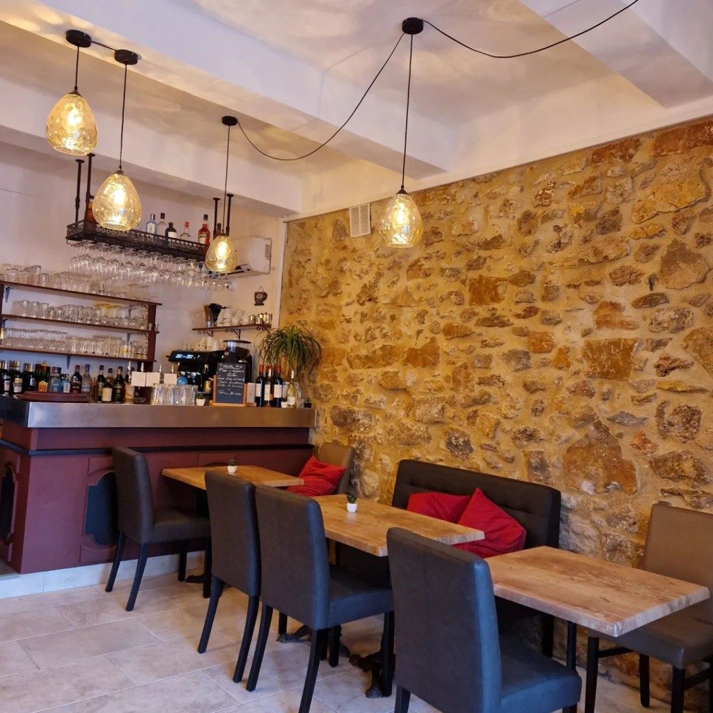 La salle de la brasserie : mur en pierre apparente, tables dressées et suspensions
